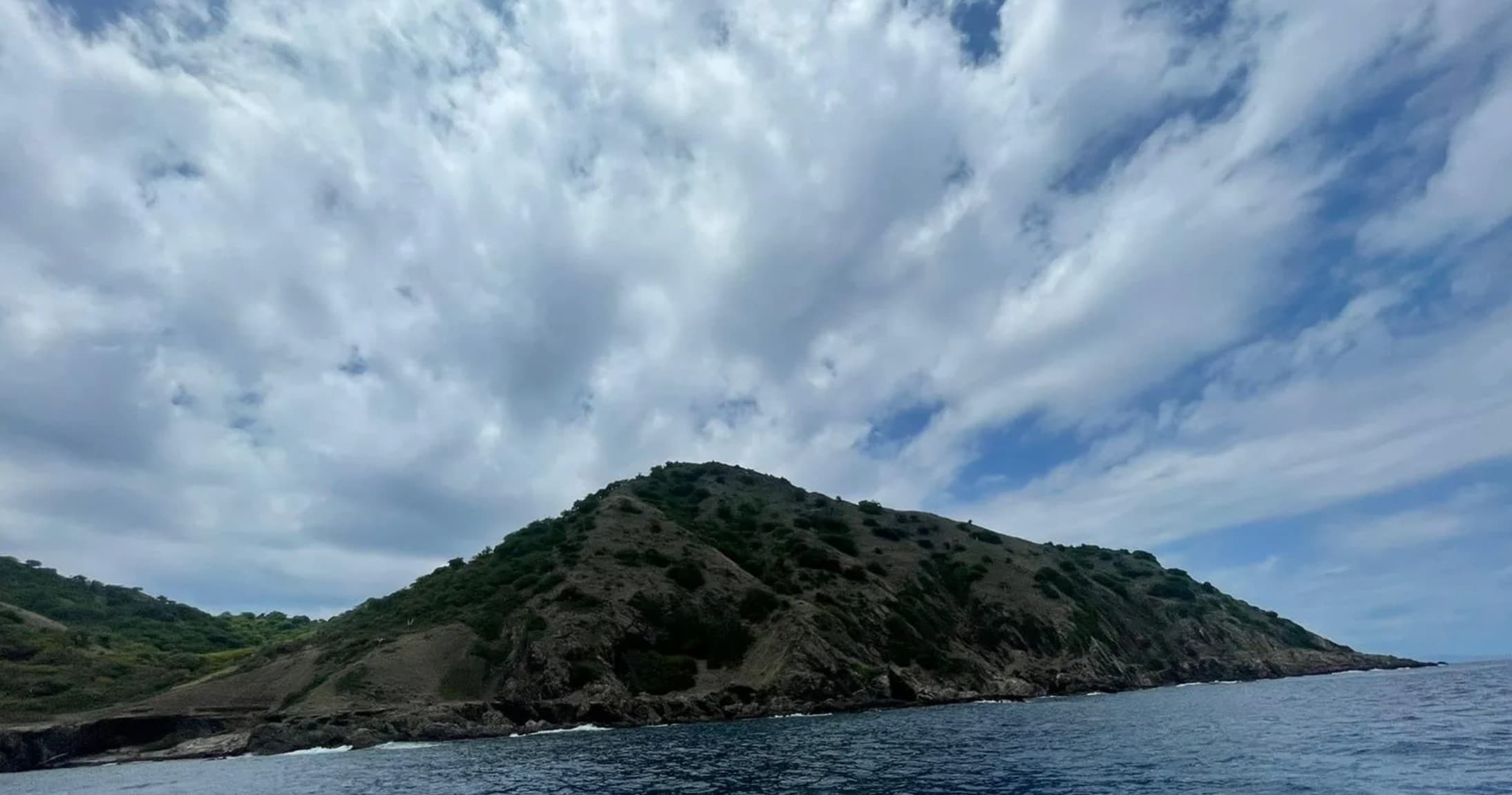 Boat trip past rocky island under dramatic cloudy sky