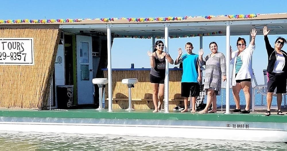 Tiki cruise passengers waving on open-deck boat at sea