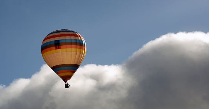 Hot air balloon drifting above dramatic cloudscape over countryside