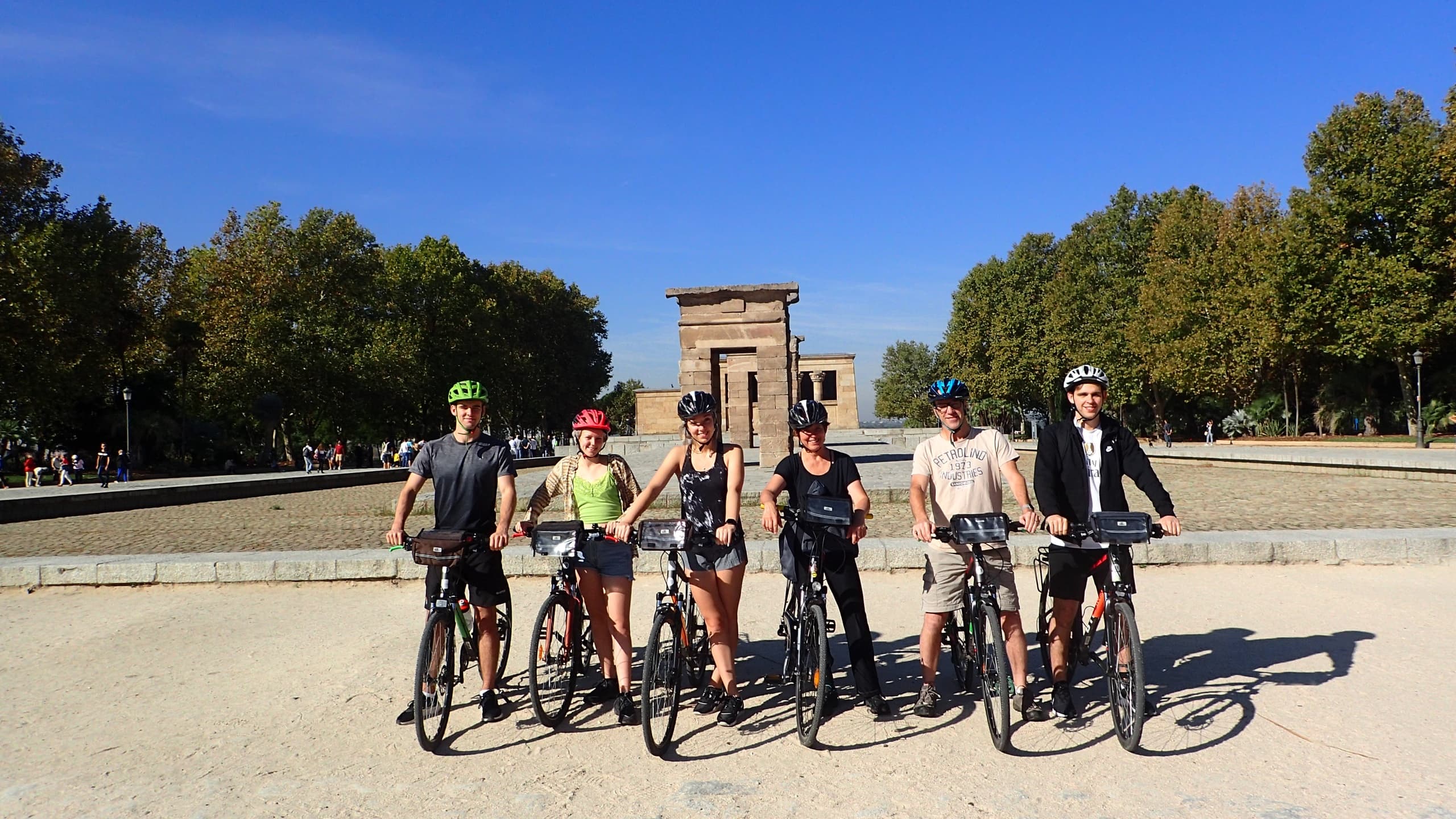 Bike tour group posed at historic park monument under blue sky