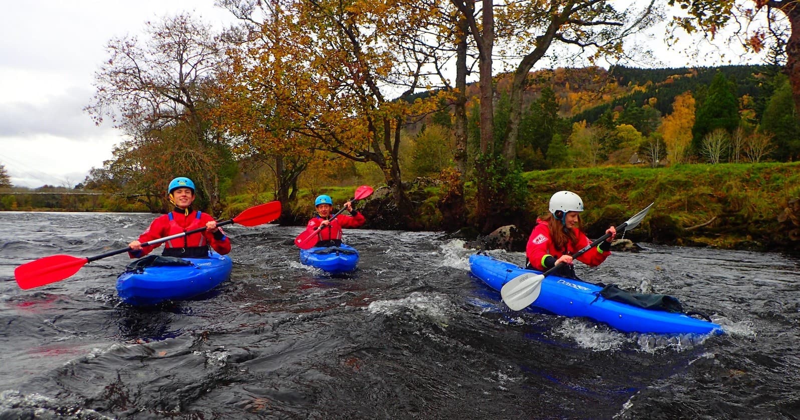 Three kayakers paddling rapids on a scenic wooded river outing