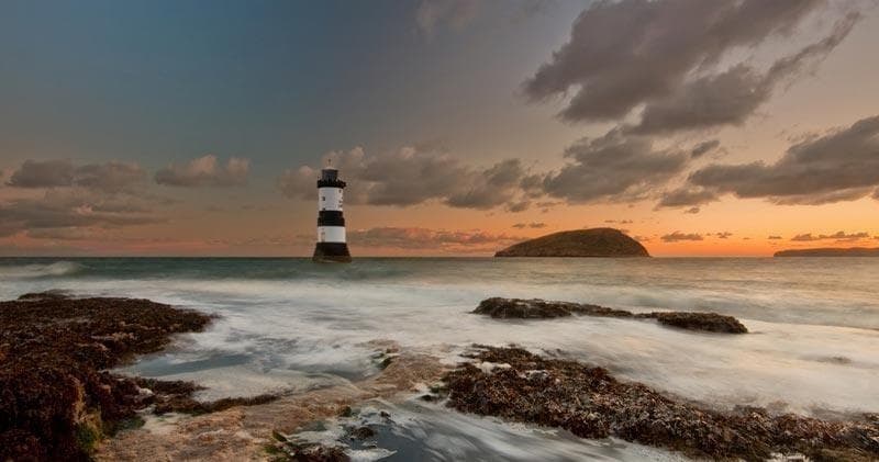 Lighthouse at sunset on rocky coast, dramatic coastal seascape