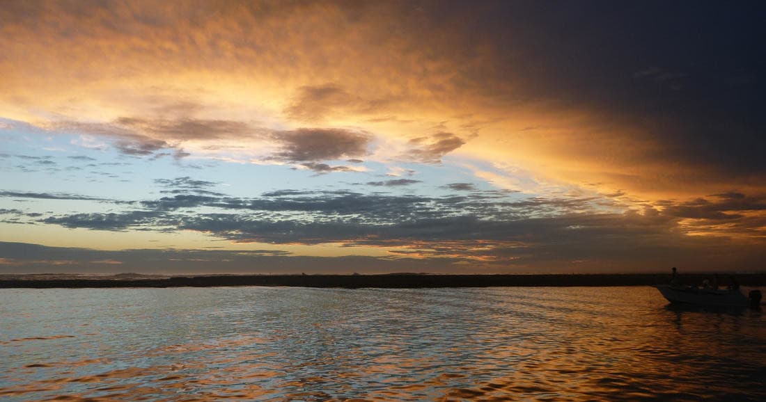 Orange sunset over open water with distant shoreline, tranquil seascape