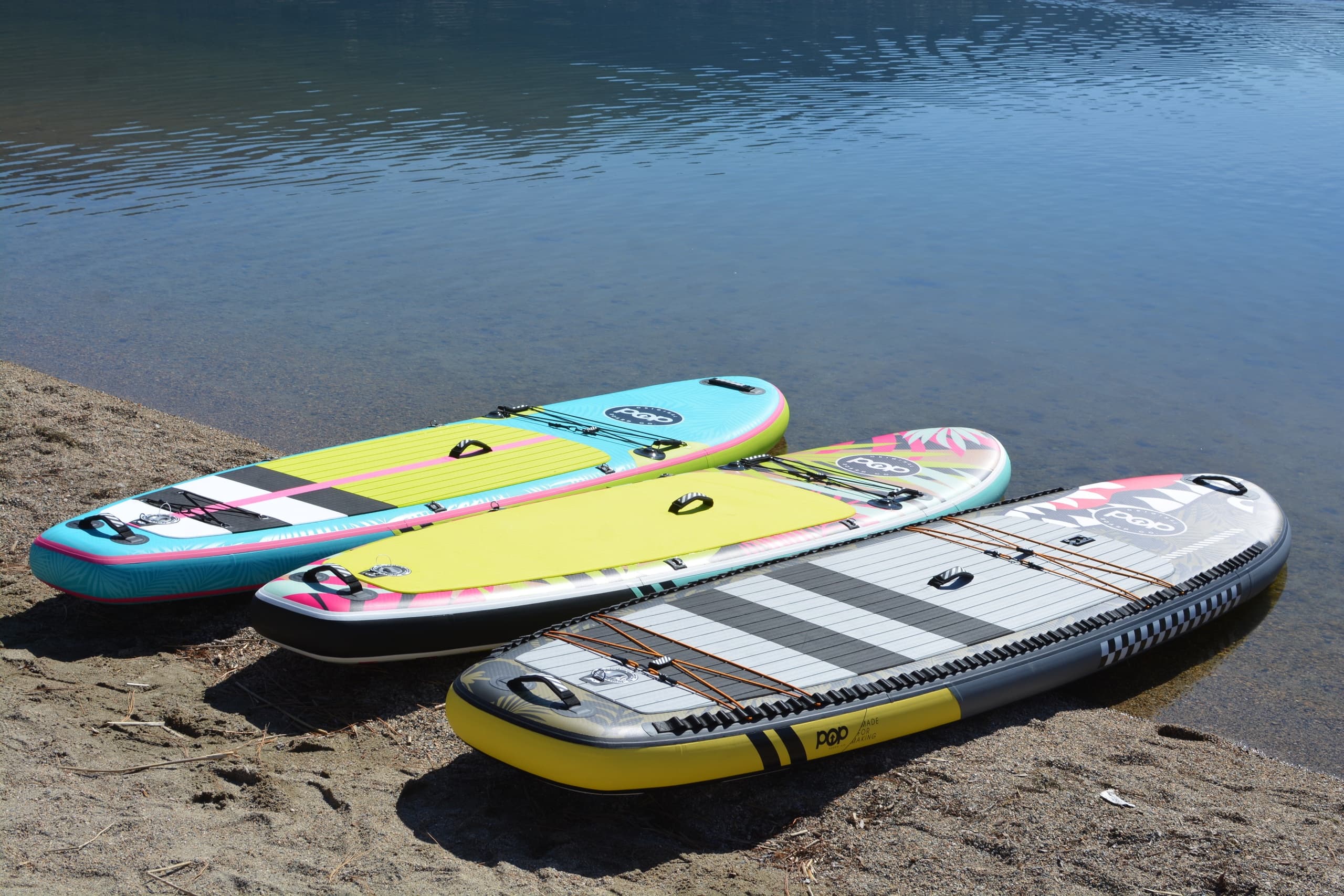 Three colorful paddleboards resting on sandy lake shore