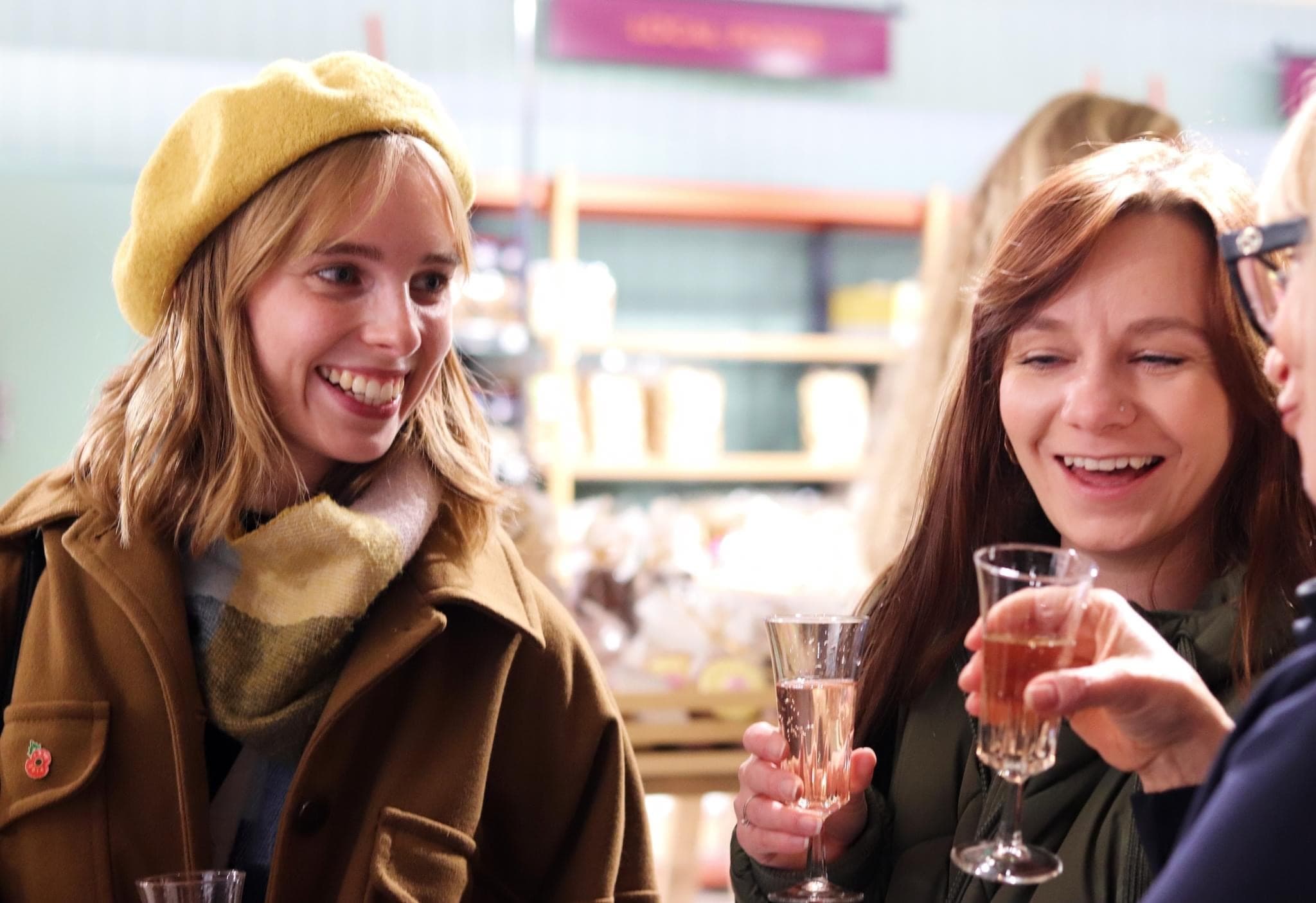 Women sampling drinks and smiling at indoor market tasting