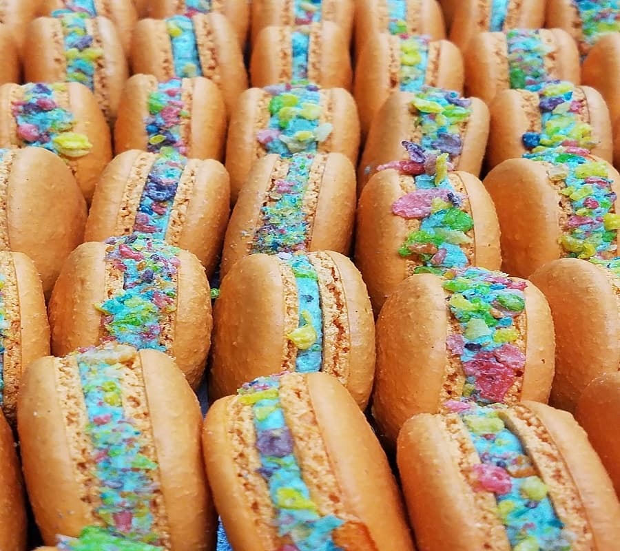 Caramel macarons filled with colorful cereal in pastry tray