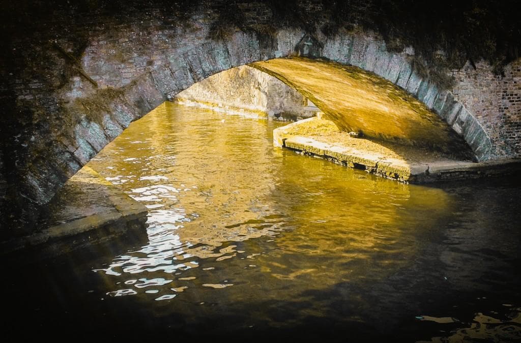 Golden light under old stone canal bridge in atmospheric Bruges