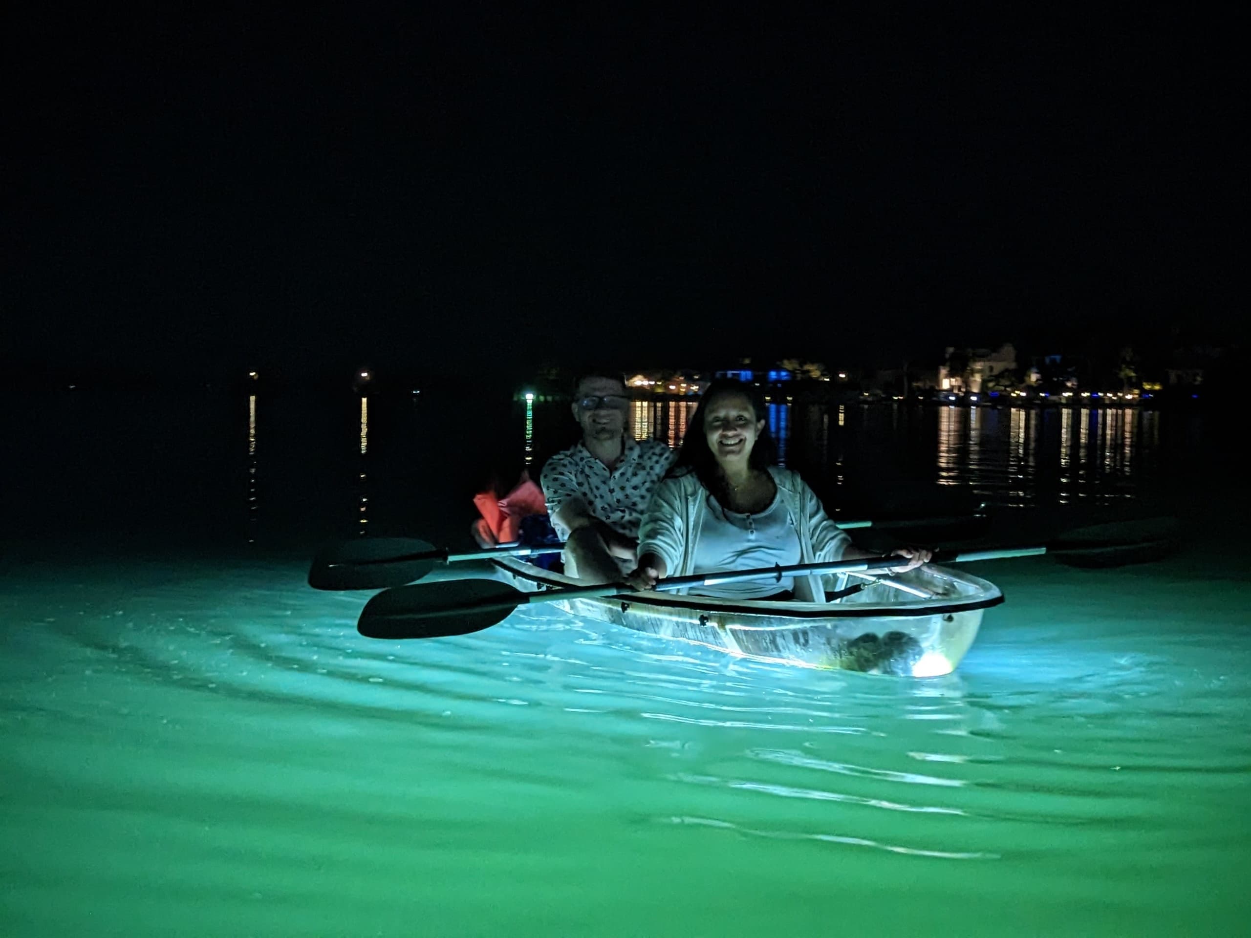 Couple in clear kayak on glowing water at night, coastal tour