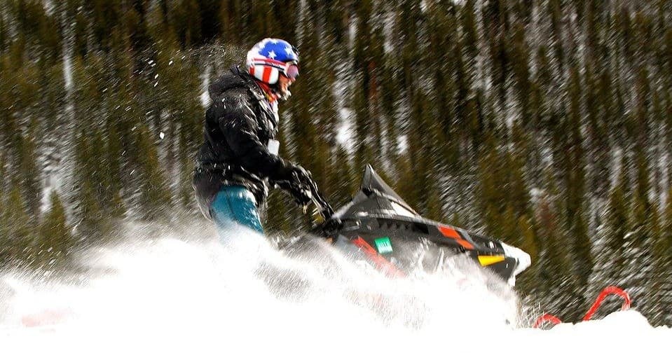 Snowmobiler carving through powder with pine forest backdrop