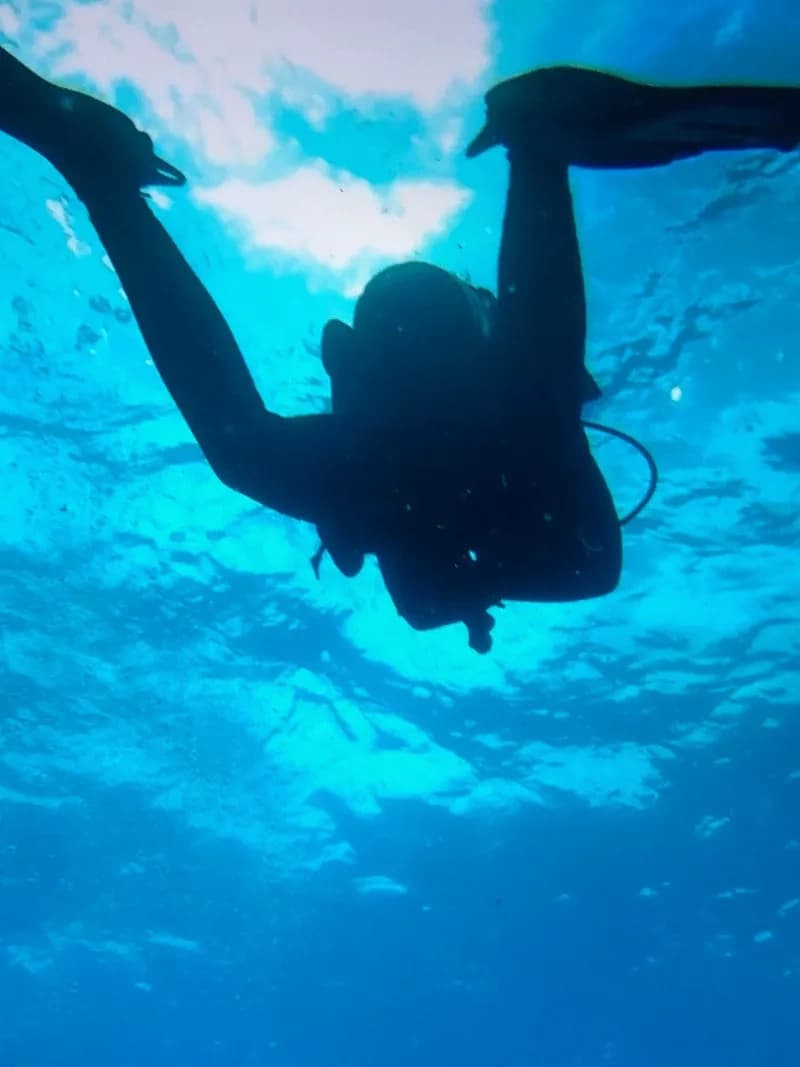 Scuba diver silhouette ascending under tropical blue water