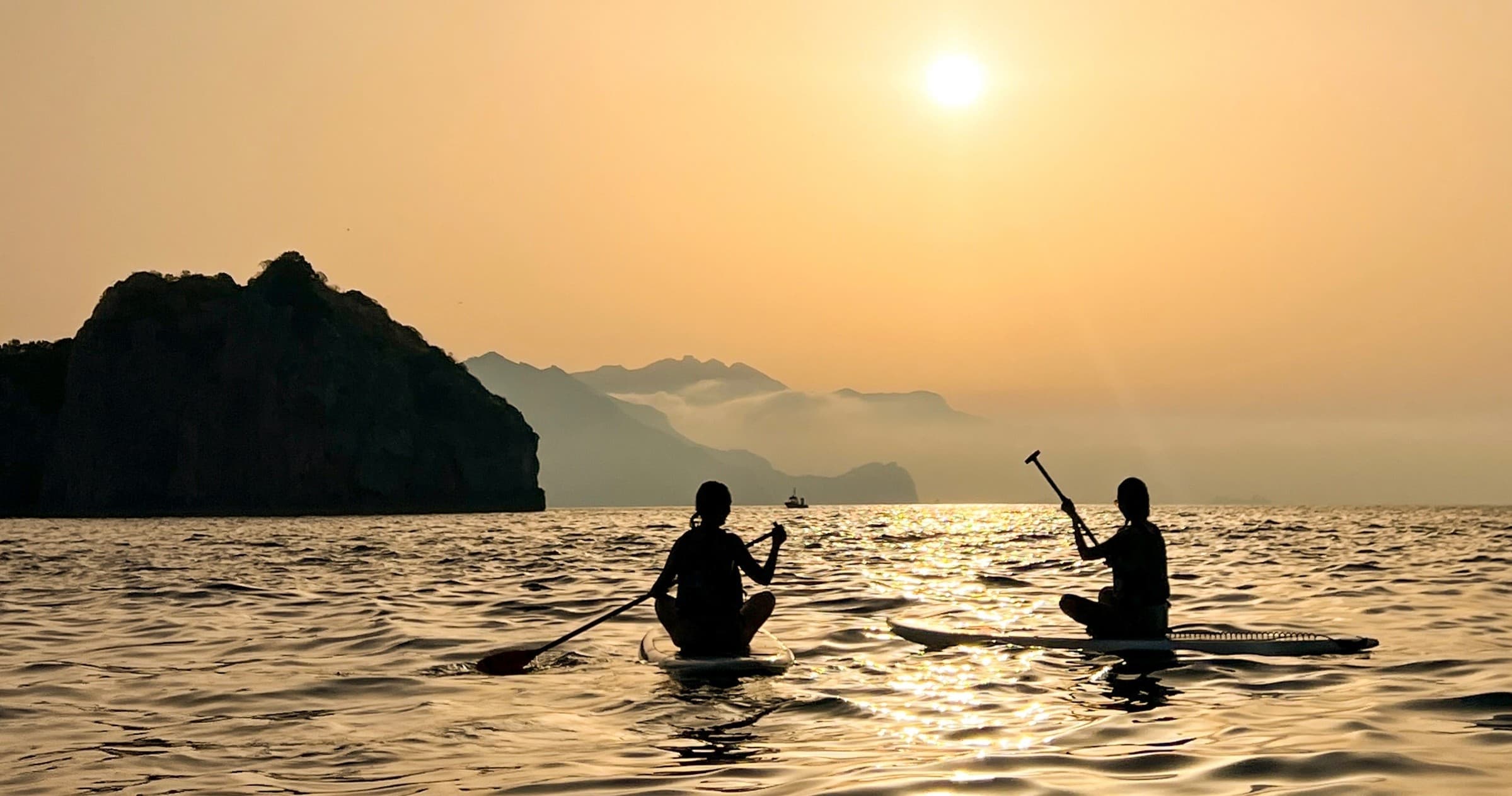 Two kayakers silhouetted at sunrise paddling near coastal cliffs