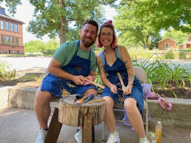Couple carving wooden spoons outdoors at park carving demo