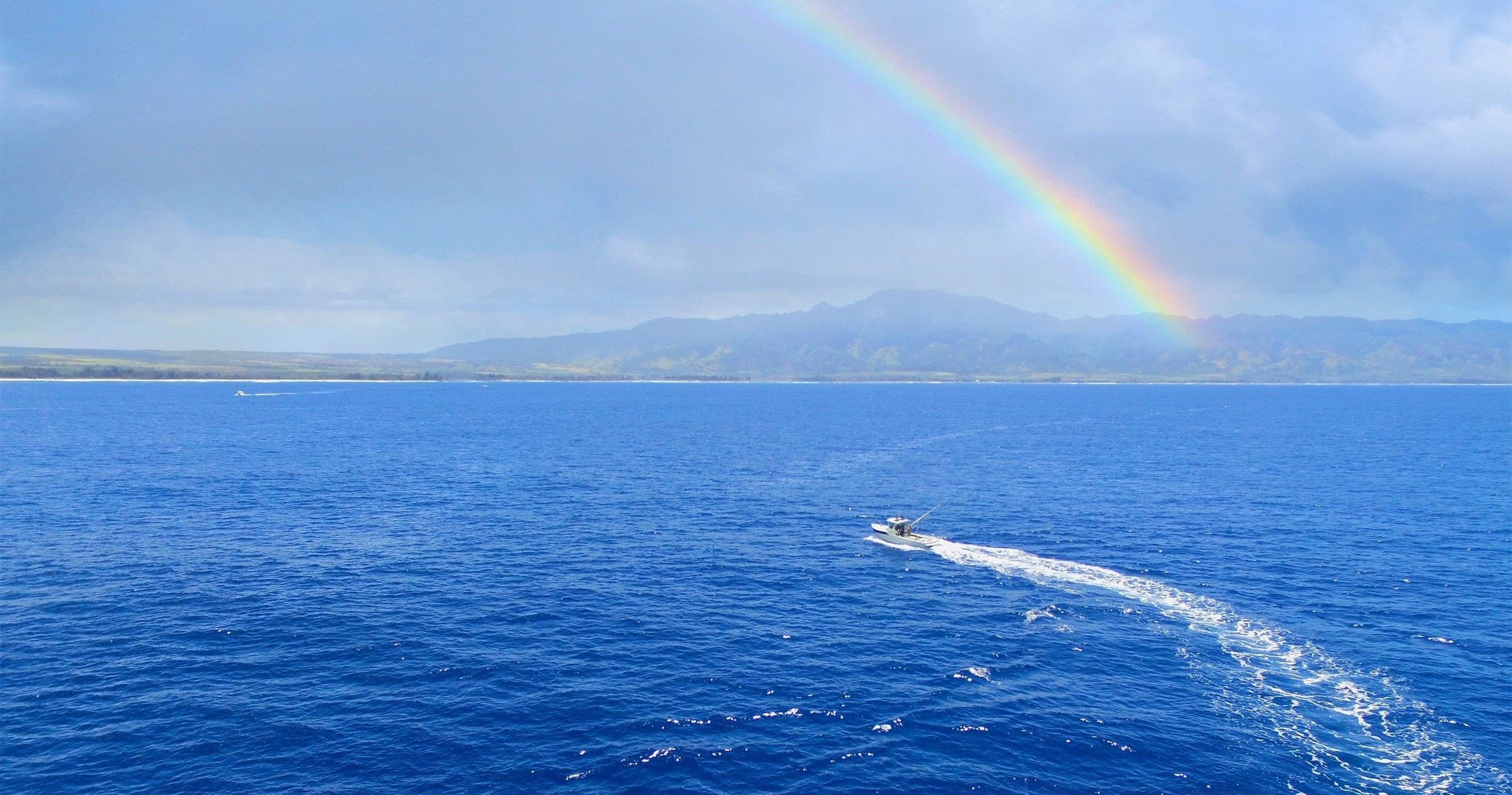 Boat cruising under rainbow over open ocean near coast