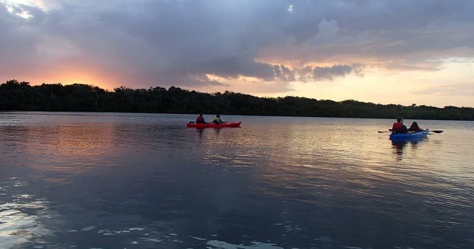 Kayakers paddling at sunset over calm coastal bay waters