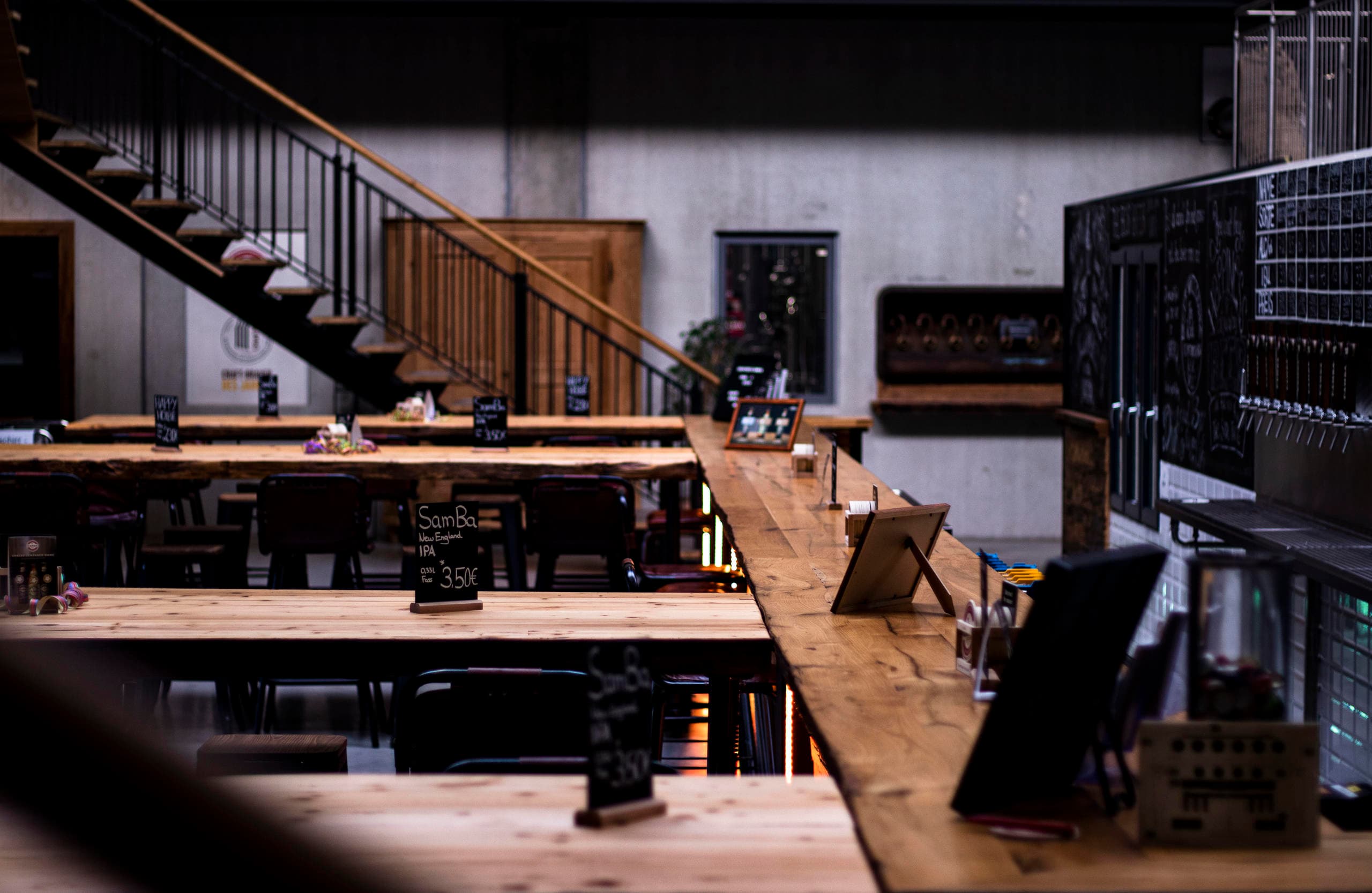 Spacious brewery taproom with long wooden tables and stairs