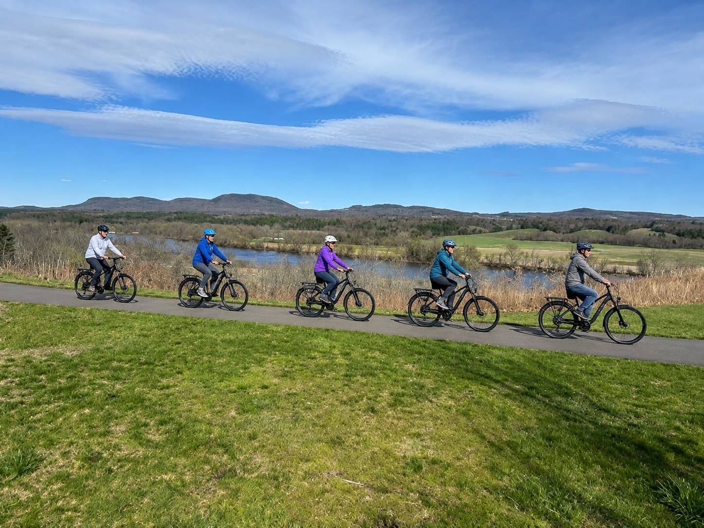 Group of cyclists riding scenic lakeside trail with mountains