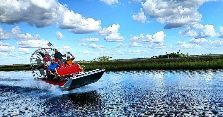 Airboat skimming marsh channels under blue skies, adrenaline ride