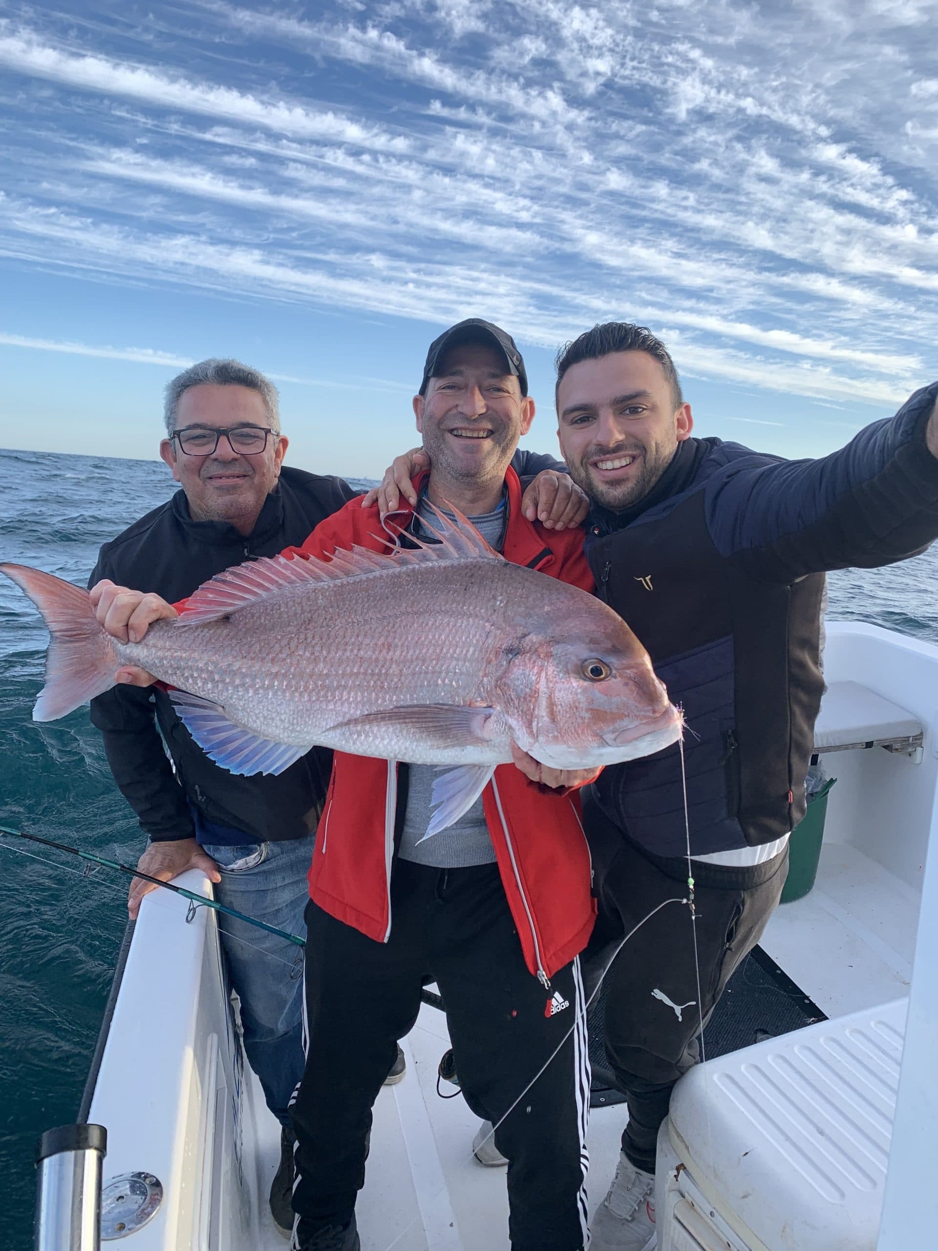 Three fishermen posing with trophy snapper on open ocean charter