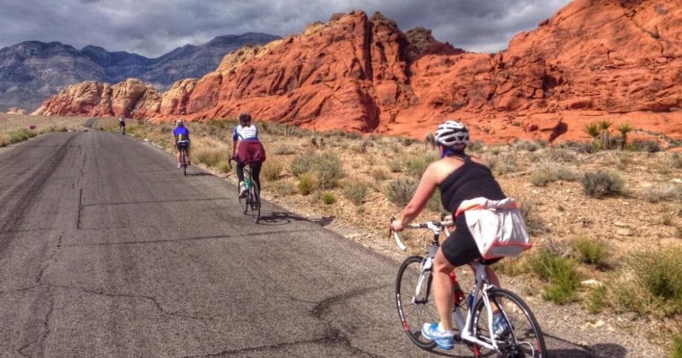 Road cyclists riding past red rock formations in desert