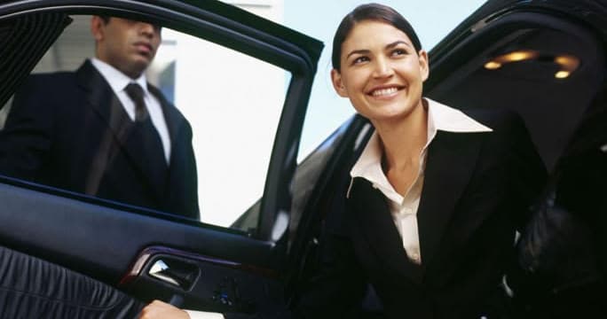 Professional chauffeur assisting passenger exiting sedan in urban setting