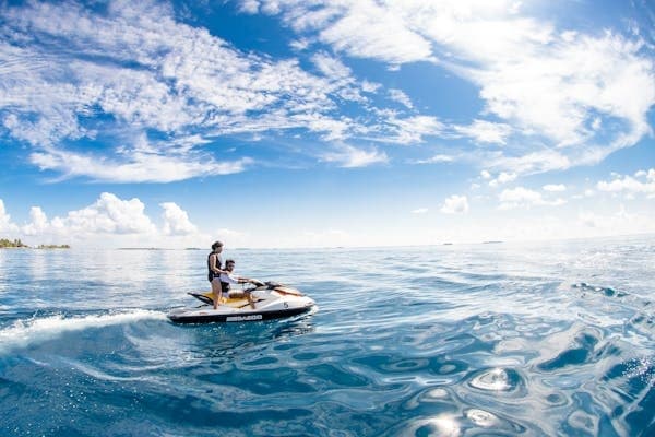 Person riding jet ski on crystal ocean near tropical coastline under blue sky