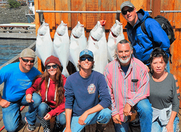 Group of anglers posing with halibut on dock at an Alaska fishing lodge