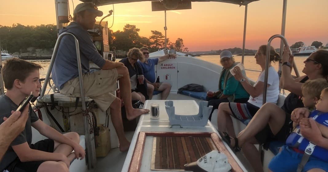 Group sailing trip aboard open-deck boat at sunset, passengers chatting