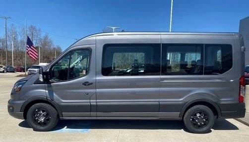 Side view of gray tour van parked with American flag at lot