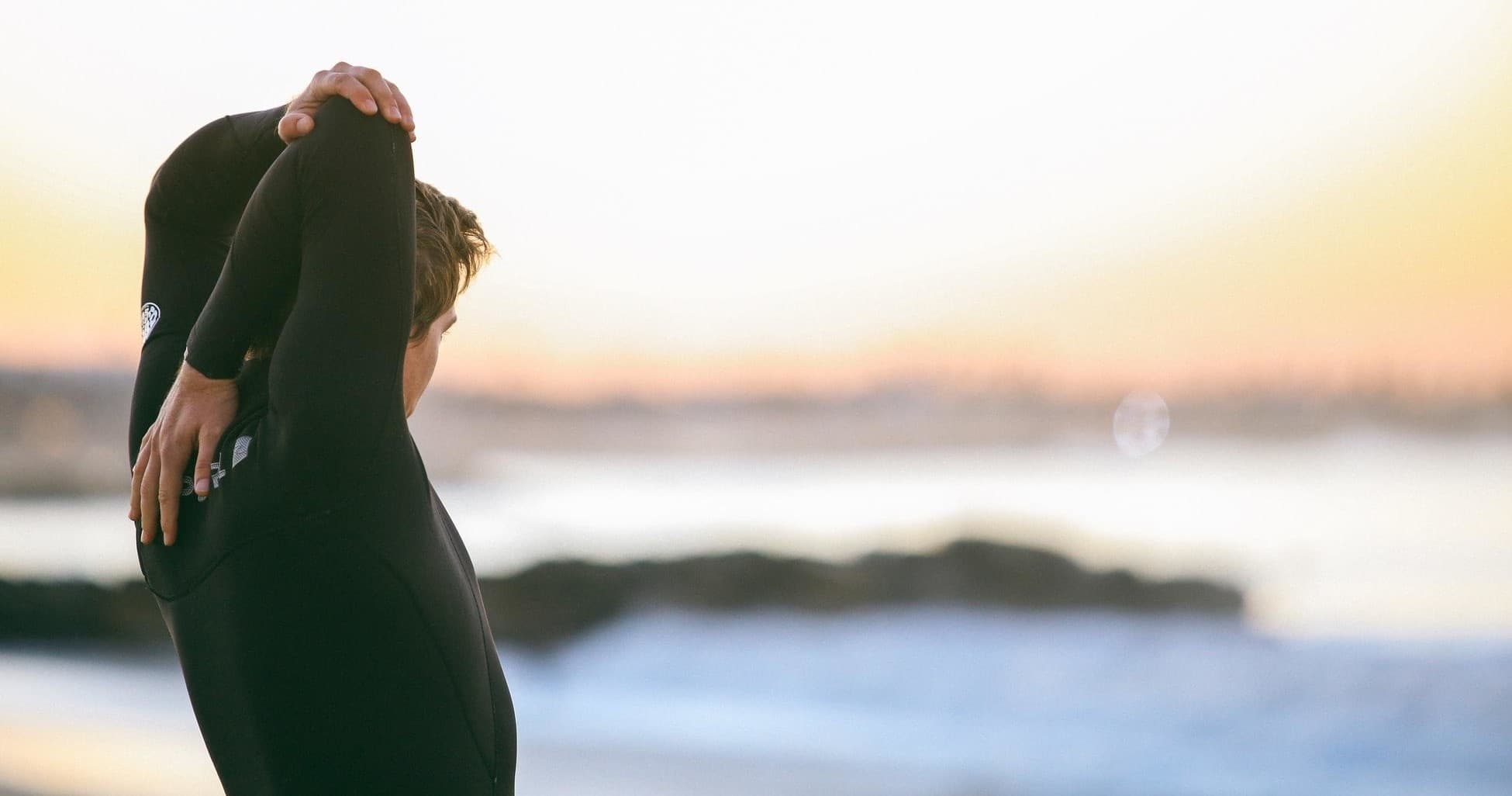 Surfer stretching in wetsuit on shoreline during golden hour