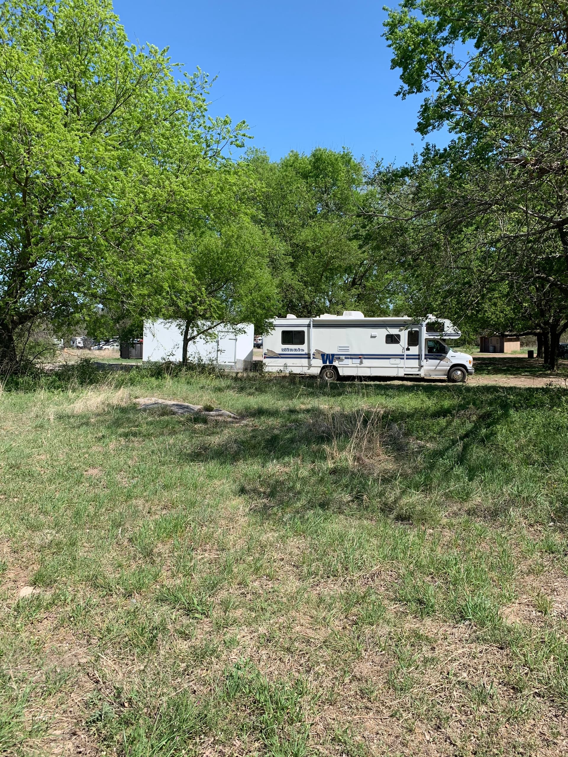 Class C RV parked under trees at shaded grassy ranch campsite
