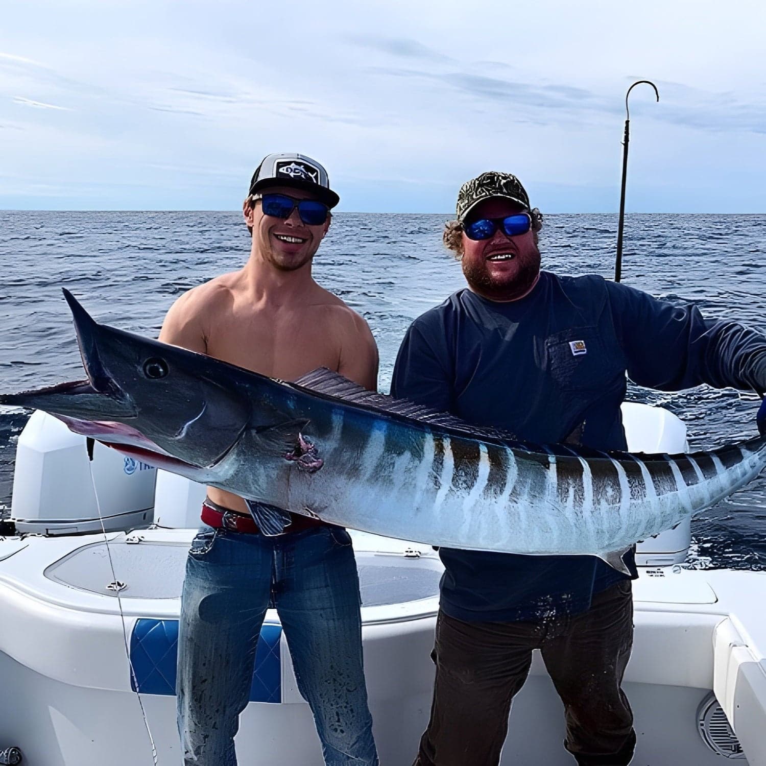 Two anglers holding large wahoo aboard offshore fishing boat
