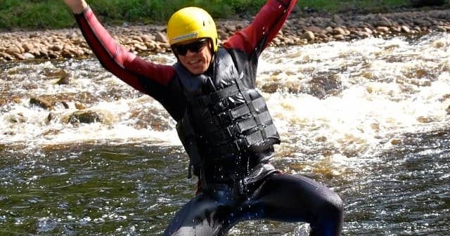 Thrilled rafter raising arms while running fast river rapids