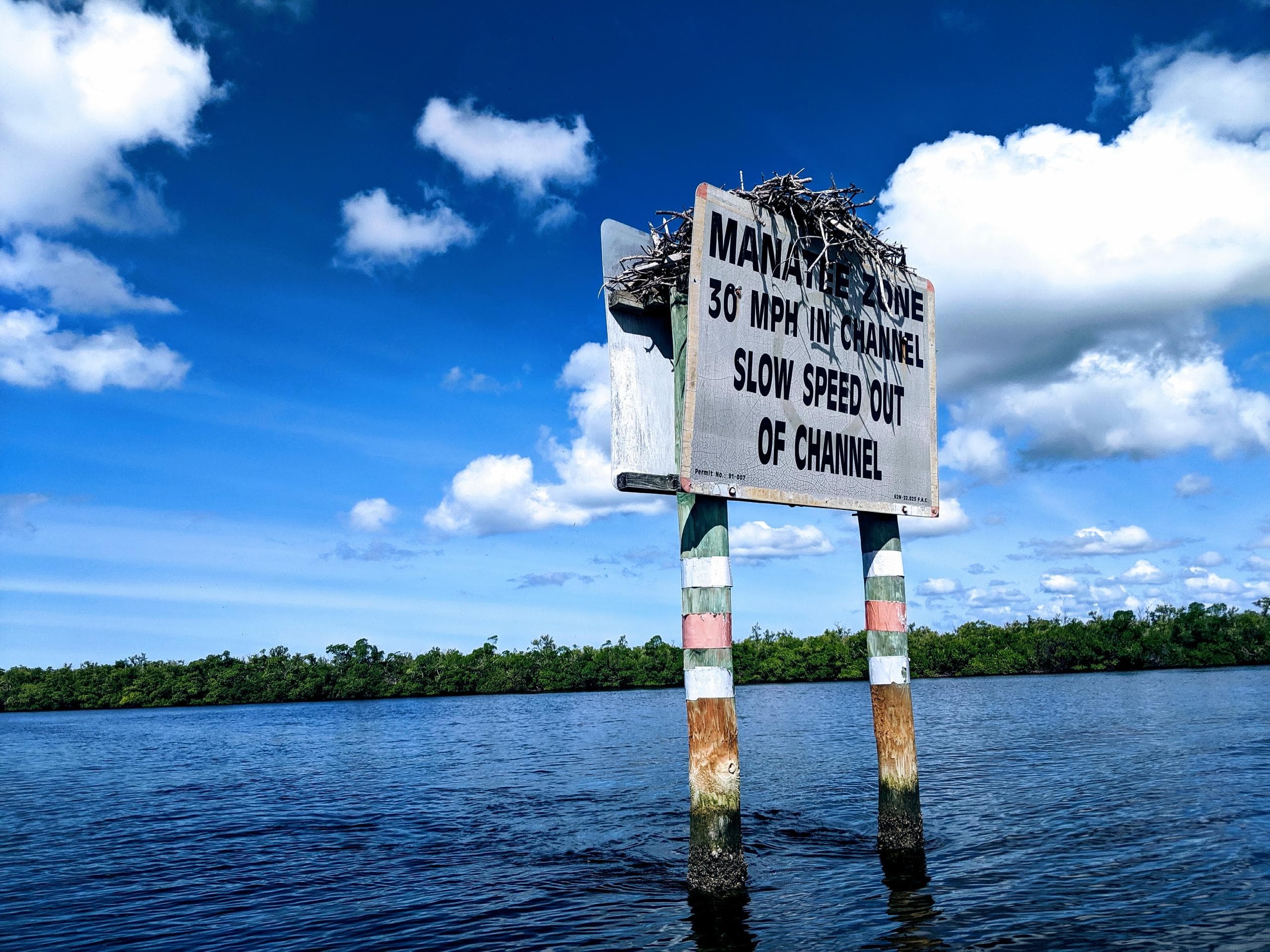 Channel speed limit sign over water, mangrove estuary entrance