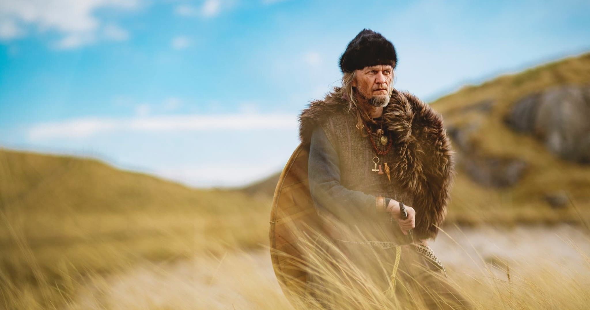 Solo Viking reenactor walking dunes on grassy coastal hillside
