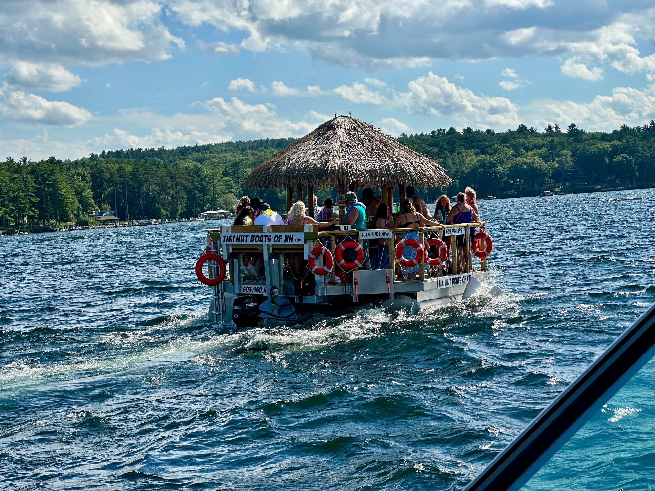 Tiki pontoon boat cruising across blue lake with thatch roof