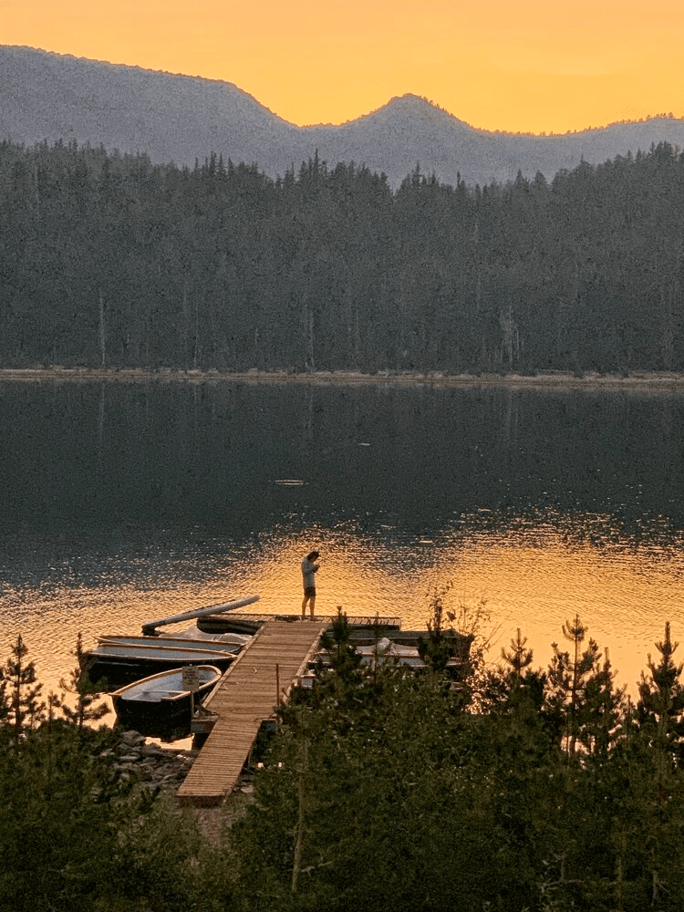 Sunset dock with lone angler on mountain lake, golden light