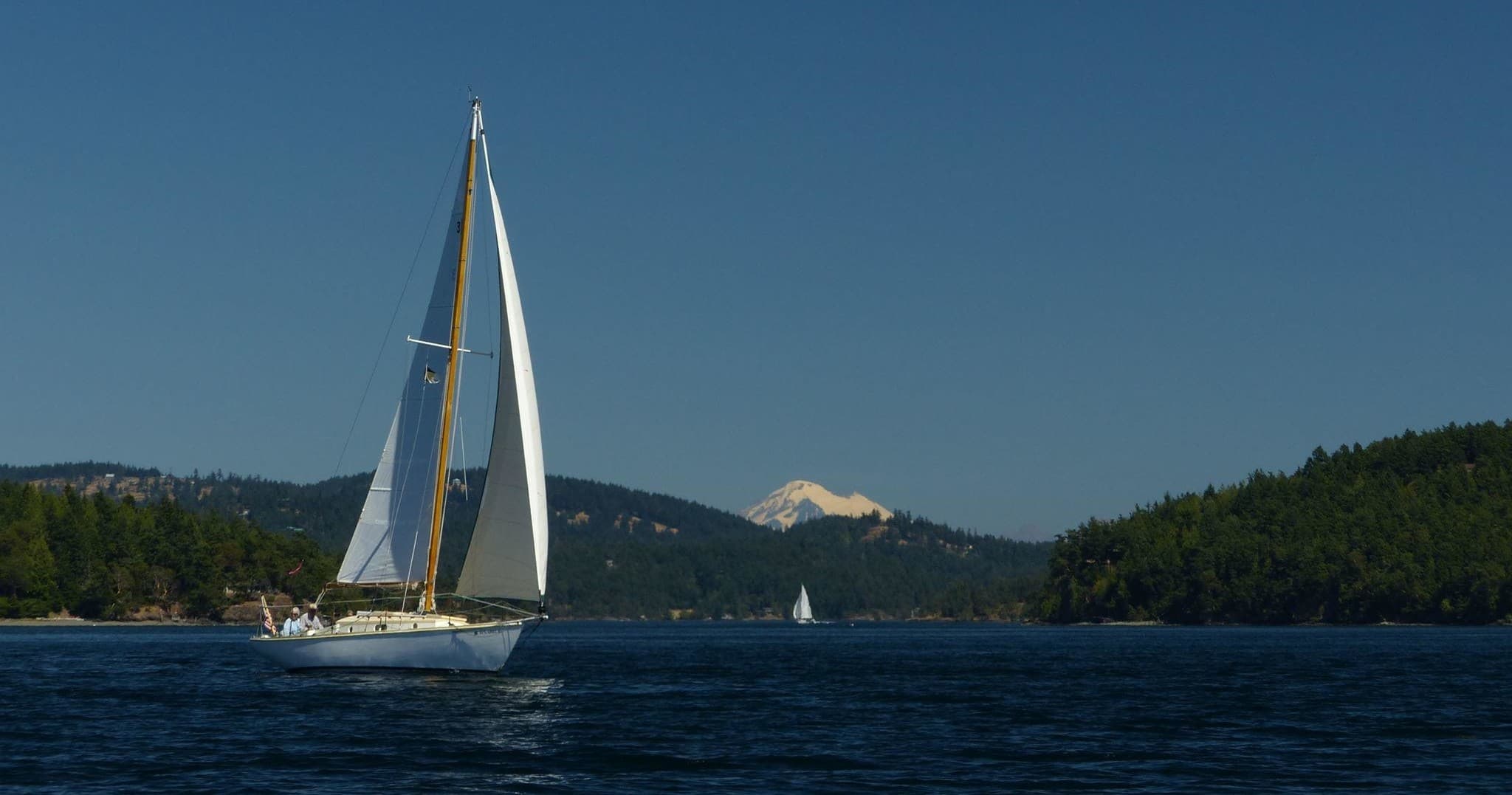 Sailboat cruising past forested islands with mountain view