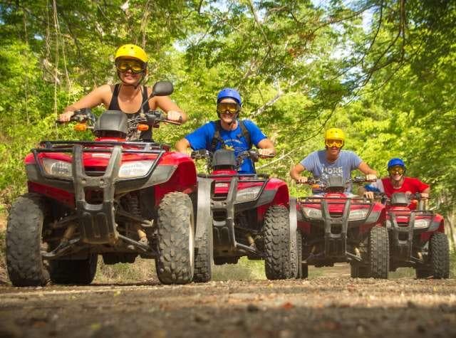 Group riding ATVs on forest trail through lush tropical jungle