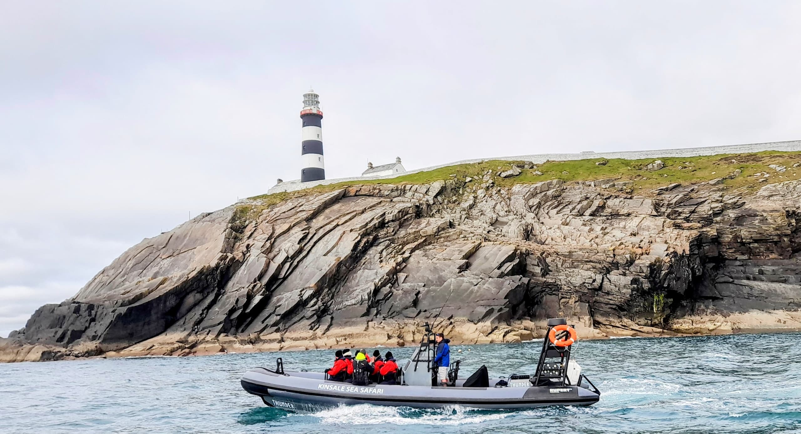 RIB sea safari boat cruising past rocky lighthouse coast in Kinsale