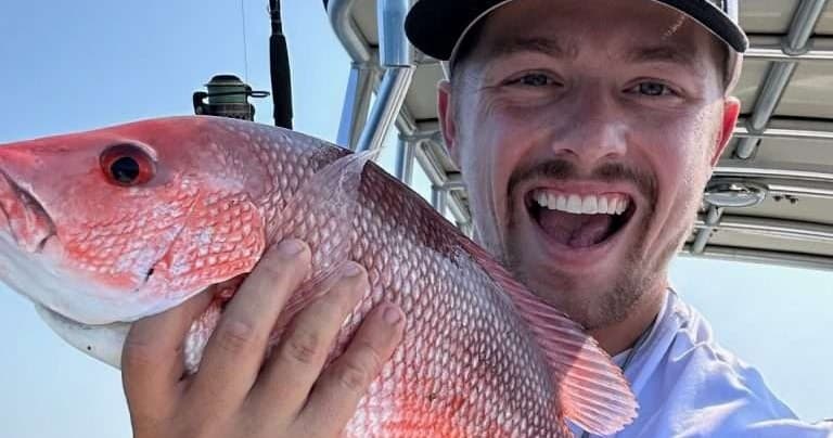 Angler selfie holding red snapper aboard charter boat near reef