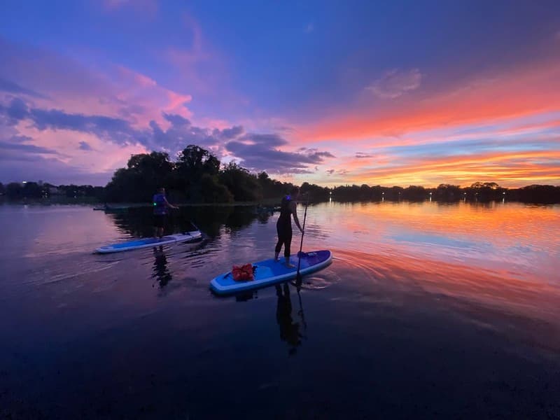 Paddleboarders gliding at colorful sunset on calm lake