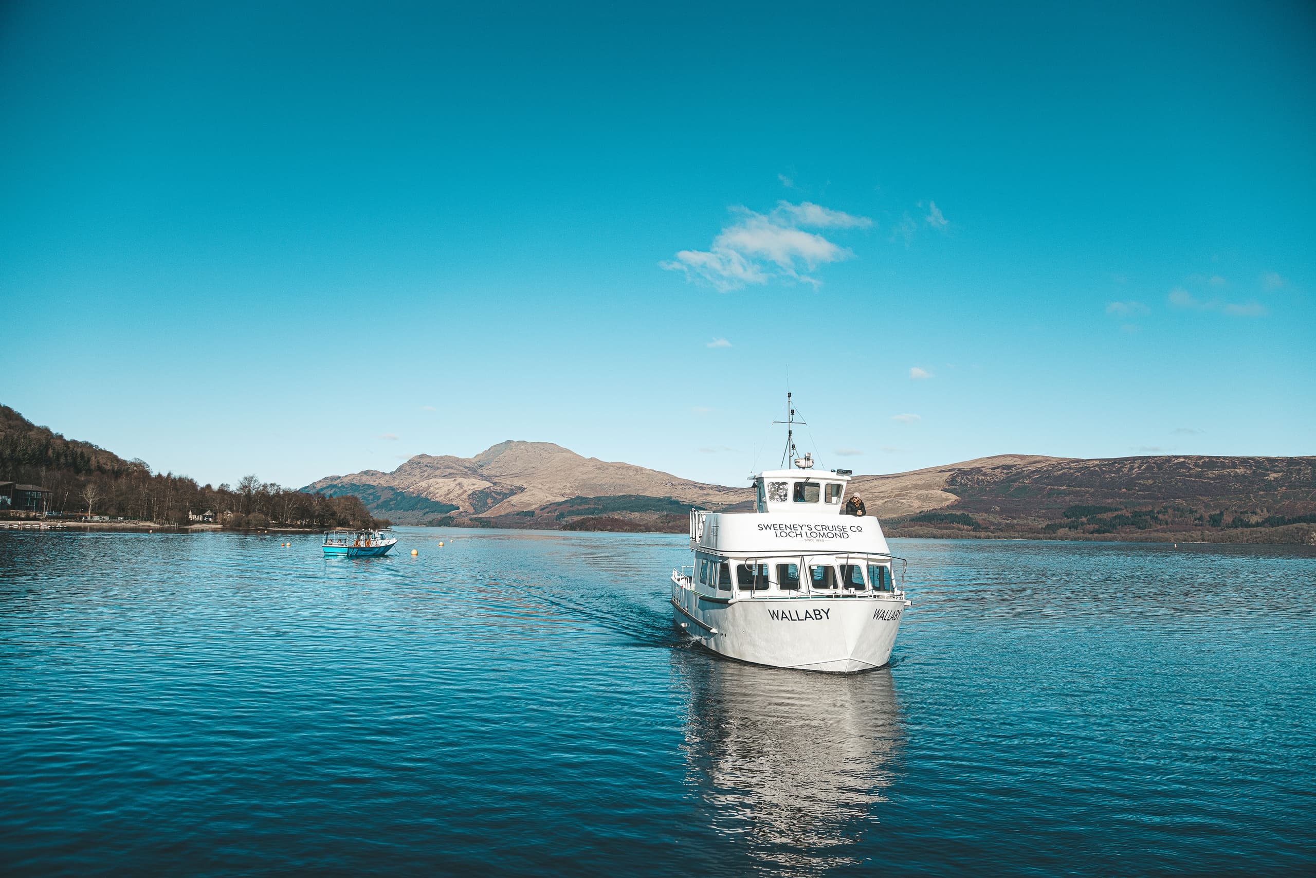 Passenger cruise boat approaching on turquoise lake with hills