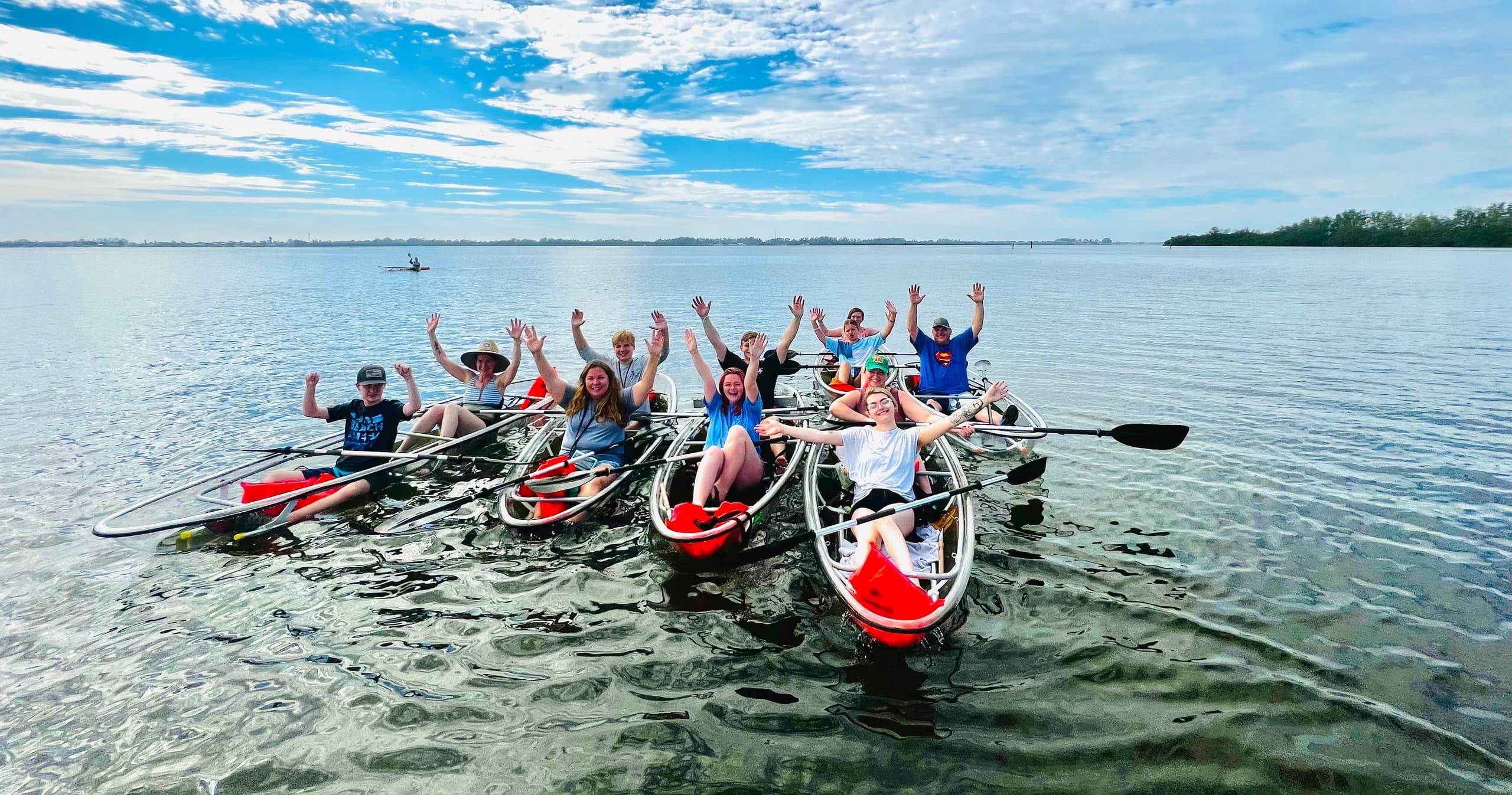 Group kayaking on clear coastal waters with sunny sky horizon