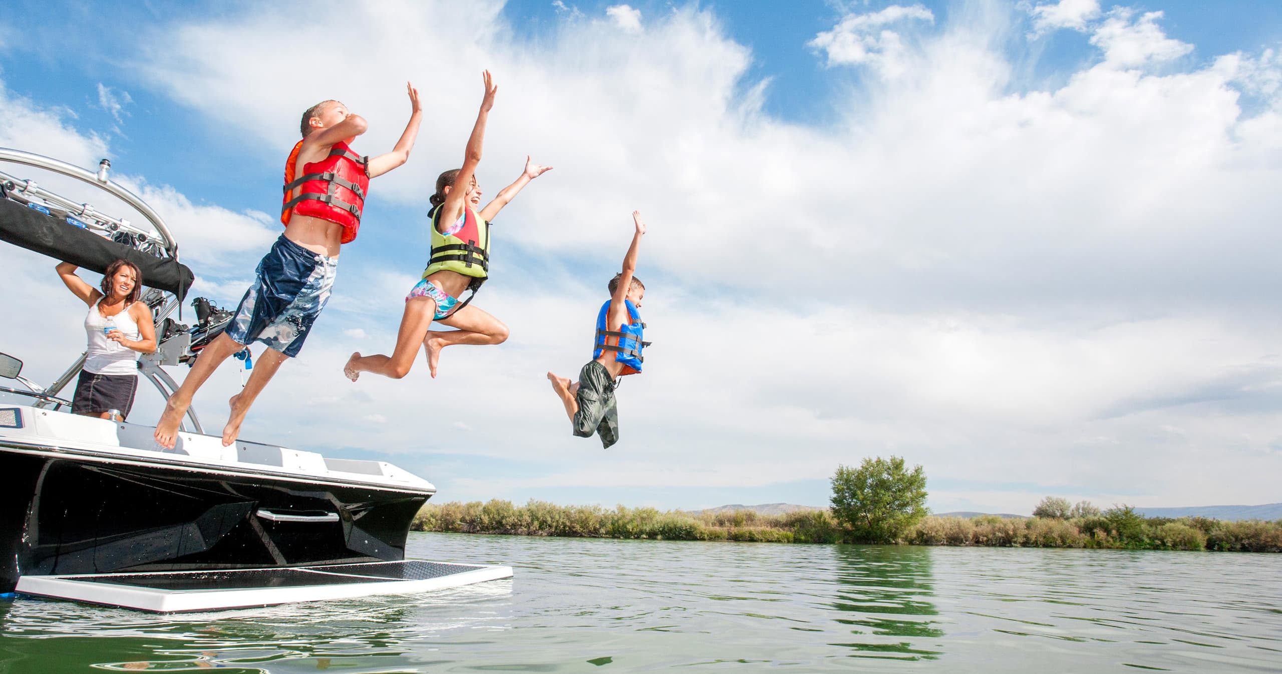 People jumping from boat into lake on sunny summer boating trip