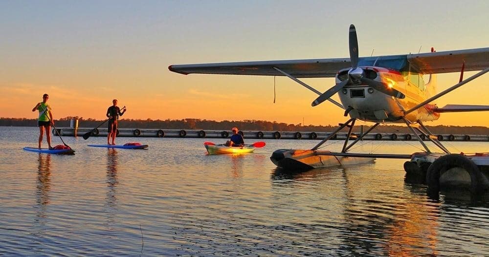 Seaplane at golden sunset with paddleboarders on calm water