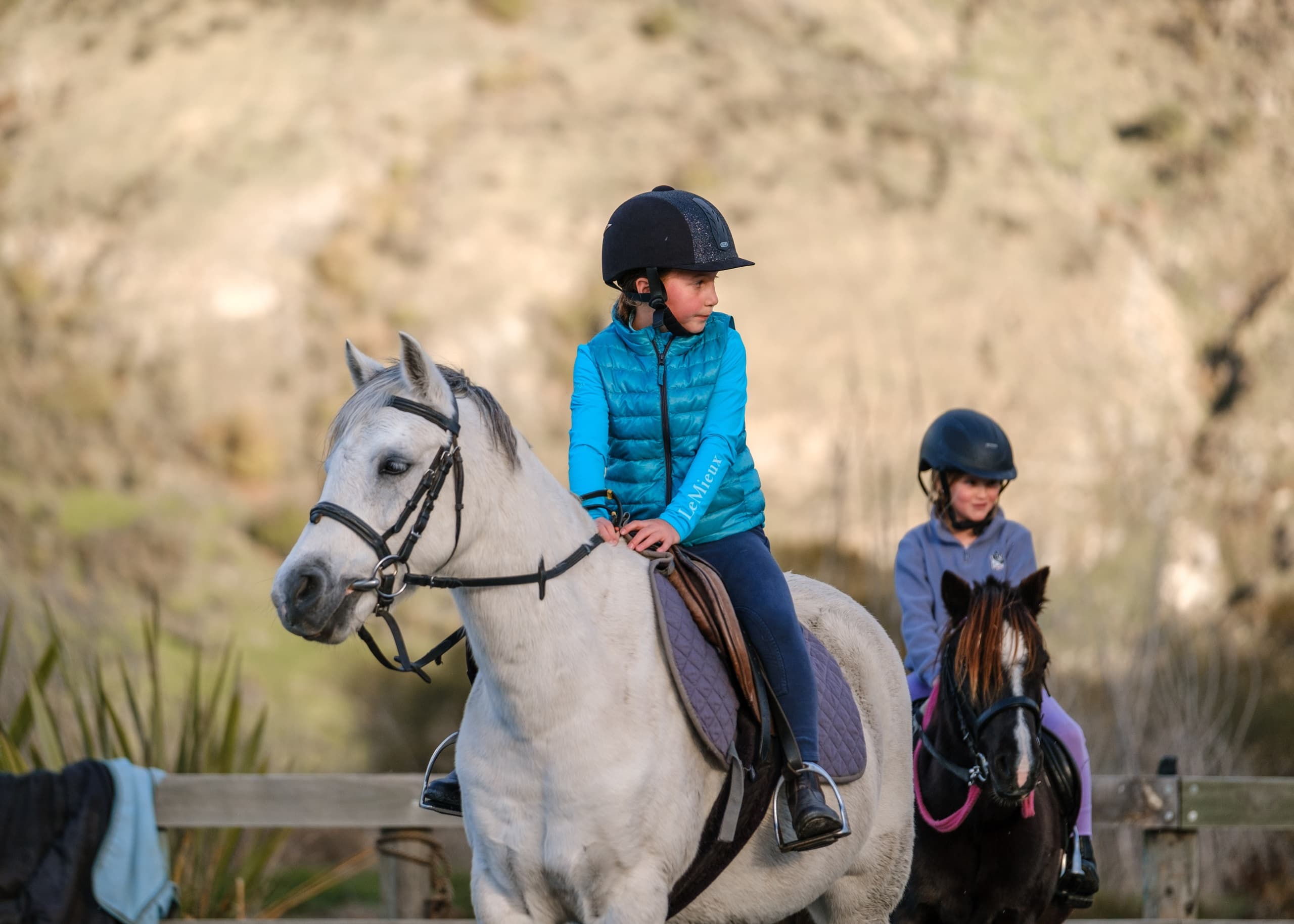 Children riding horses on countryside trail with hillside backdrop