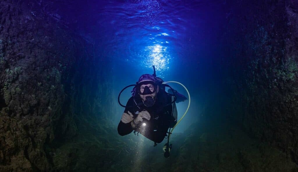 Scuba diver exploring underwater cave tunnel with light shaft