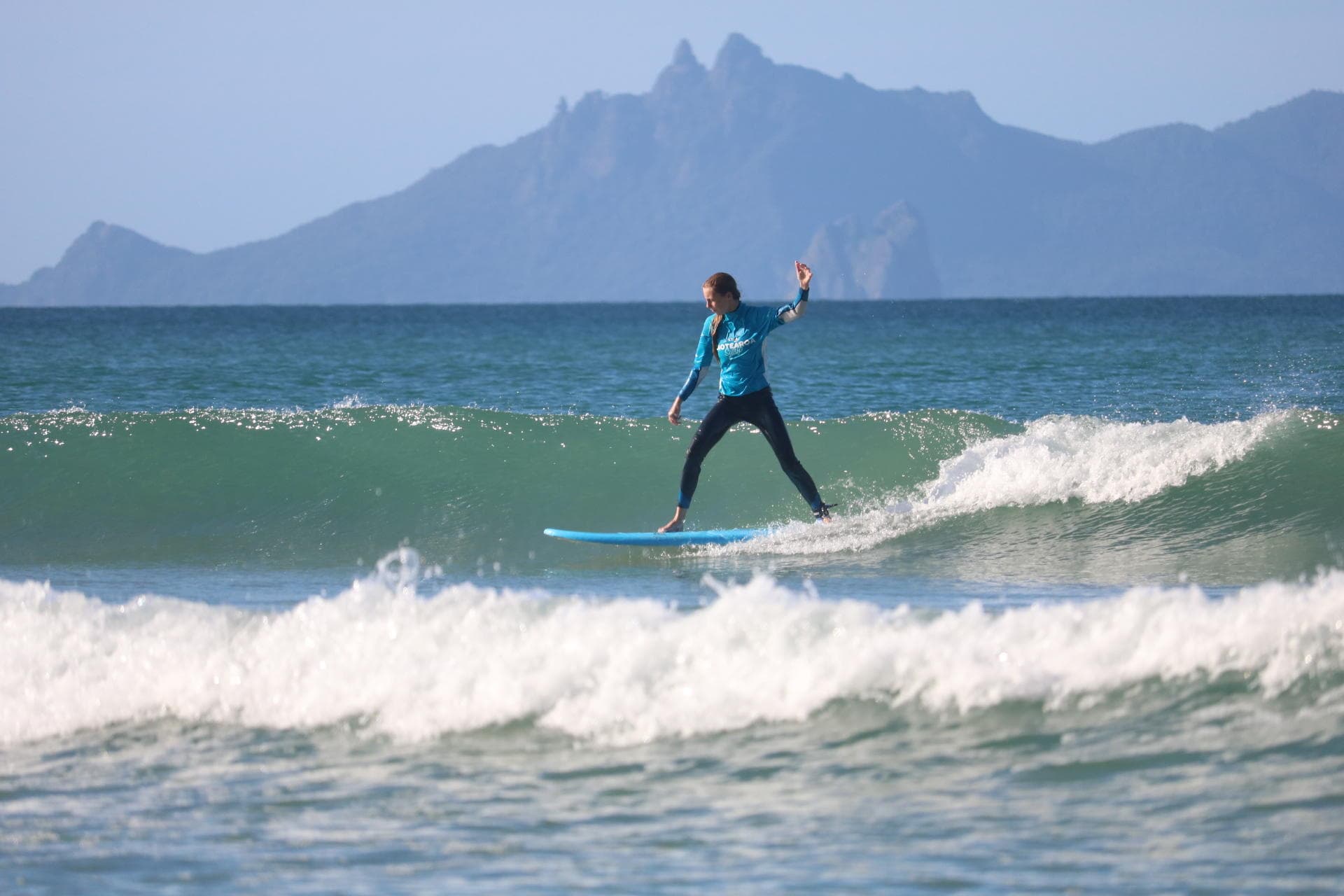 Surfer carving small wave with island and mountain backdrop