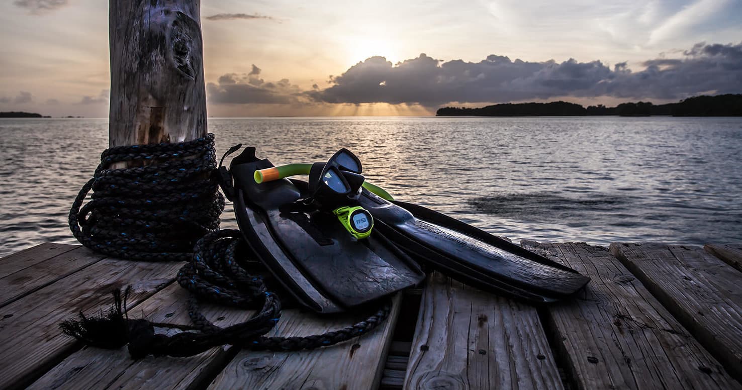 Scuba fins and mask on wooden dock at sunset over ocean