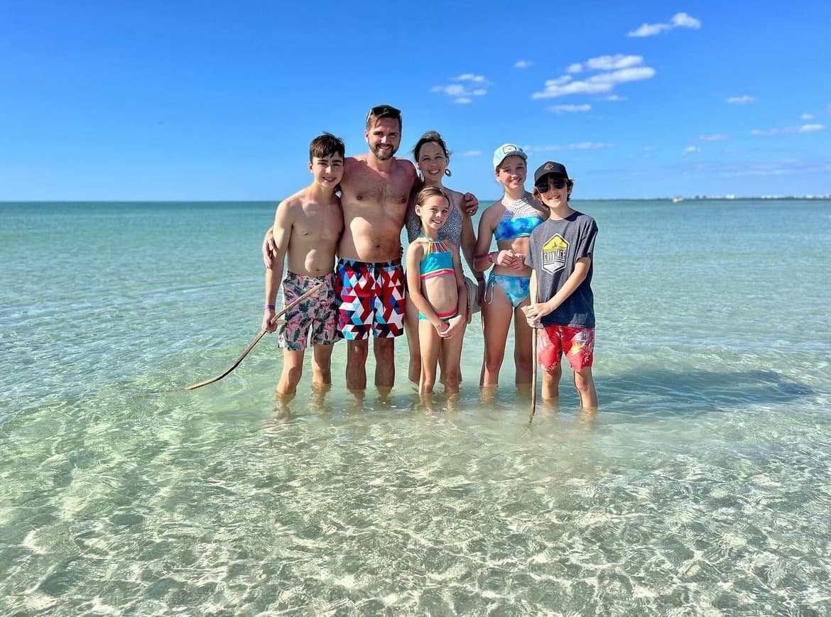 Family standing in crystal shallow water on sandy Florida beach